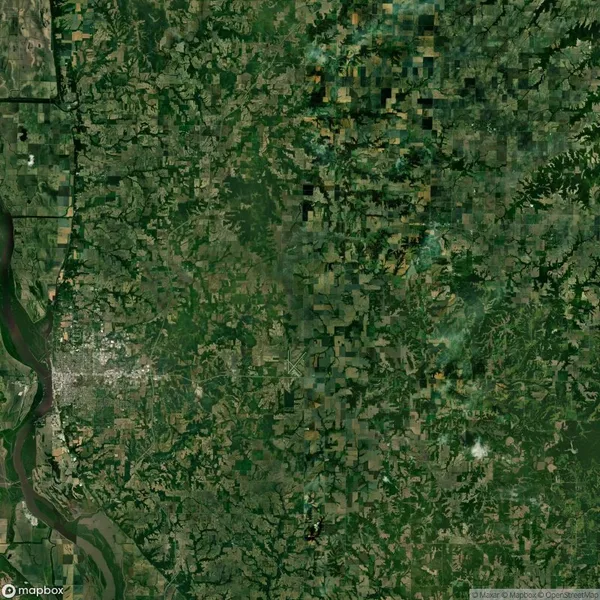 Aerial view of a rural landscape showing a patchwork of green fields, forests, and a winding river. A city area is visible towards the bottom left corner.