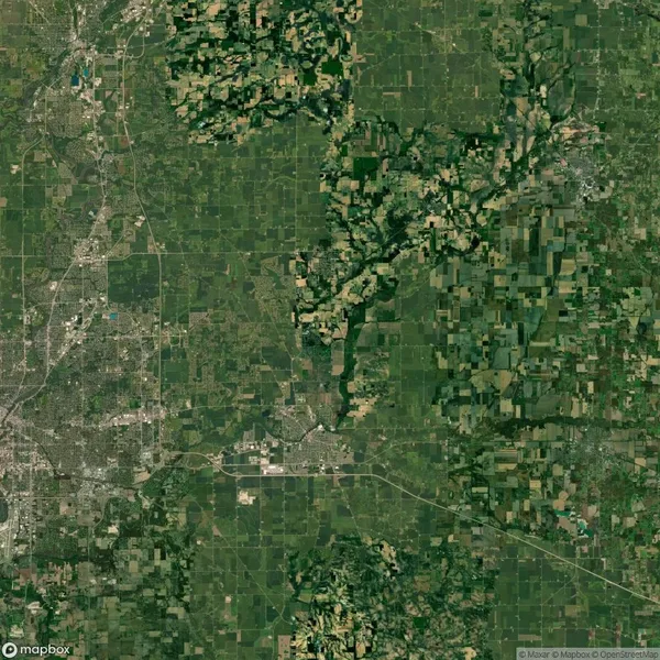 Aerial view of a lush green landscape with patchwork farmland, dense wooded areas, and a few urban developments scattered throughout.