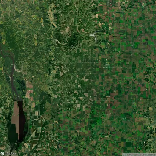 Aerial view of a landscape showing a patchwork of agricultural fields, a river on the left, and dense forest areas on the upper left.