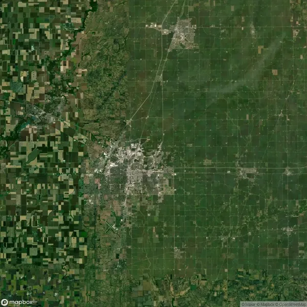 Aerial view of farmland and urban area in Nebraska. The image shows a distinct transition from green patchwork fields to a grid-like city structure.