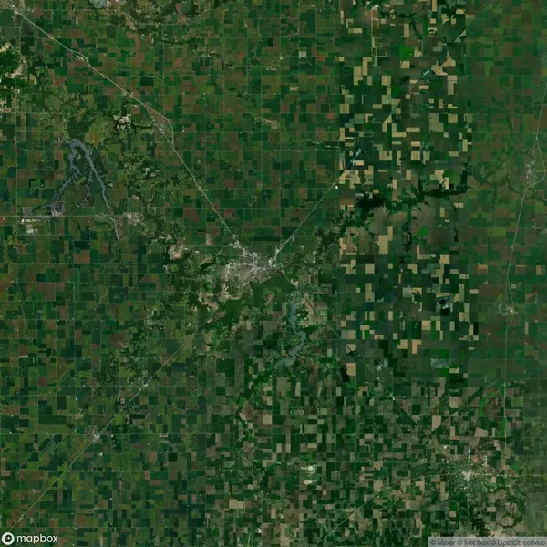Aerial view of a rural landscape with a patchwork of green and brown agricultural fields and a small town near the center.