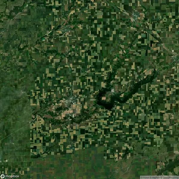 Satellite image showing a patchwork of green and brown agricultural fields, roads, a small body of water, and scattered settlements.