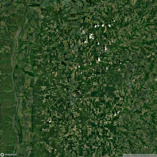 Aerial view of a vast, patchwork landscape with green fields, forests, and scattered clouds. A river runs vertically on the left side of the image.