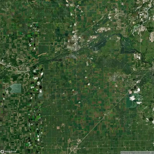Satellite view of a vast agricultural area with patchwork fields, scattered clouds, and a river running through the landscape. Roads and small urban areas are visible.