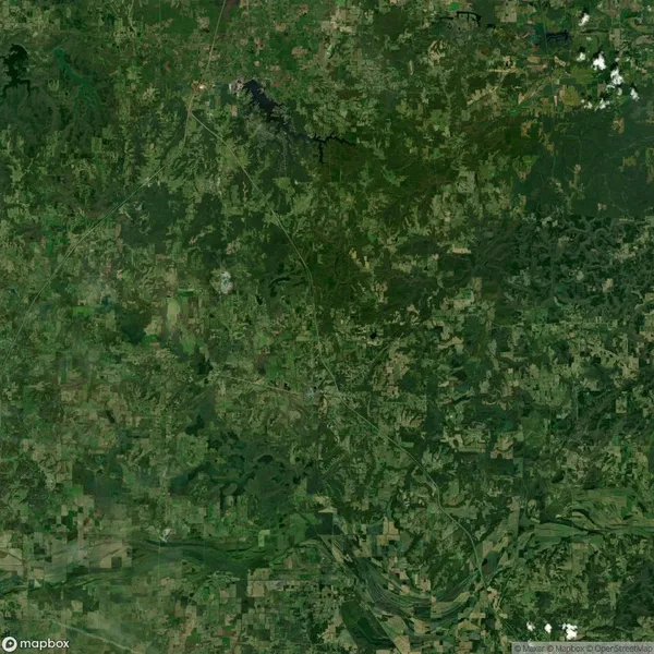 Aerial view of a rural landscape with patches of forest, fields, and a river curving through the lower part. Roads are faintly visible, indicating sparse development.