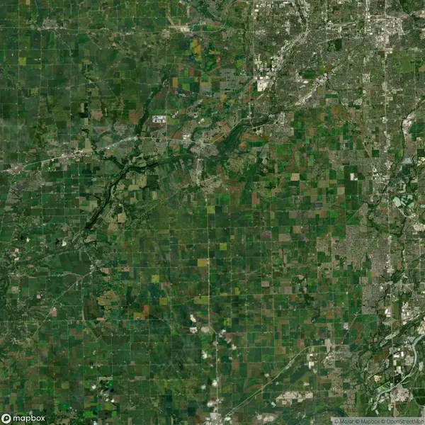 Aerial view of a landscape showing a patchwork of green fields, rivers, and roads. Urban areas are visible in the top and right sections of the image.