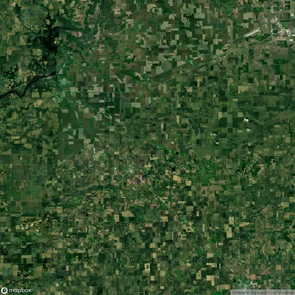 Aerial view showing a patchwork of agricultural fields and greenery, divided into various geometric shapes, with a few meandering roads and clusters of trees visible.