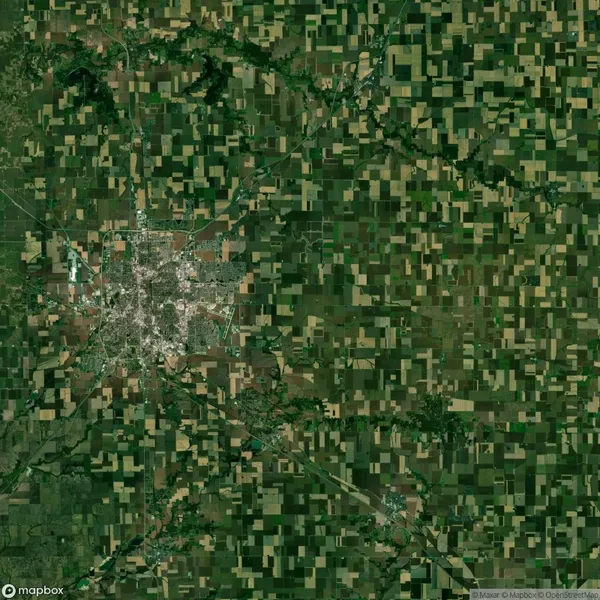 Satellite view of a rural landscape with a grid of cultivated fields surrounding a dense urban area in the center.