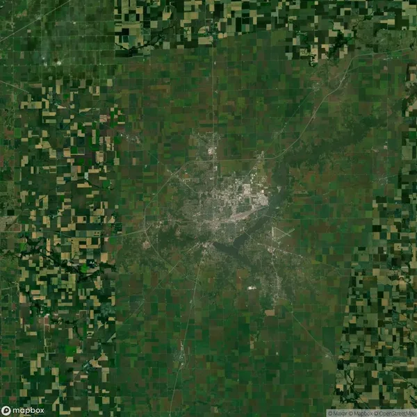 Satellite view of a city surrounded by agricultural fields, with a visible central urban area and grid-like patterns of farmland.