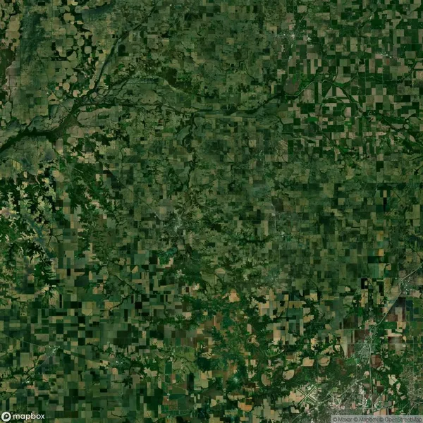 Aerial view of a large patchwork landscape showing farmland, fields, forests, and a river winding through the center. Various shades of green and brown are visible.