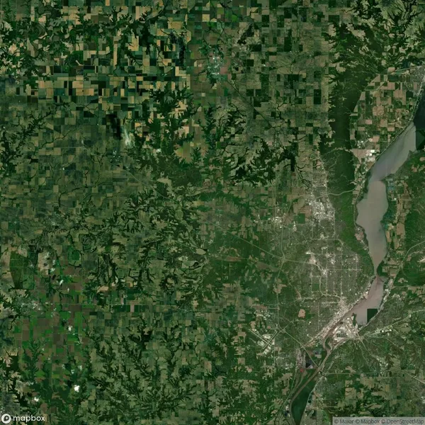 Satellite view of a landscape showing a densely forested area, a river winding through the right side, and a patchwork of agricultural fields on the left. Urban development visible near the river.