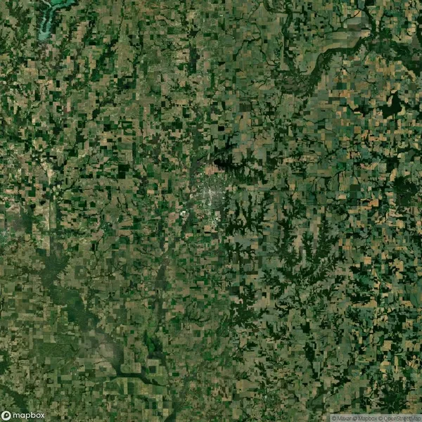 Aerial view of a rural landscape with a patchwork of green and brown fields, intersected by roads and scattered trees.