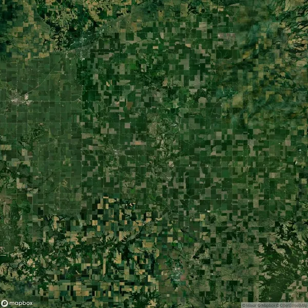 Aerial view of a patchwork landscape composed of green and brown agricultural fields arranged in a grid pattern, interspersed with patches of forested areas.