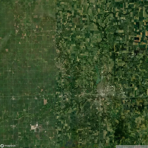 Satellite view showing a patchwork of agricultural fields and a developed urban area with roads and buildings concentrated on the right side.
