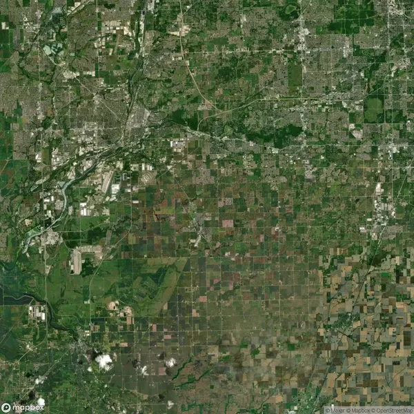 Aerial view of a grid-like landscape with urban and rural areas, roads, and patches of green and brown fields.