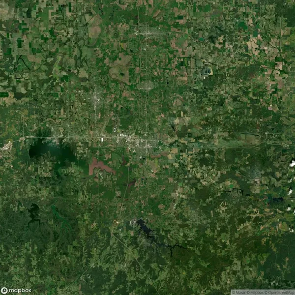 Satellite image showing a densely wooded and green landscape with some scattered clearings and developed areas, bisected by roads.