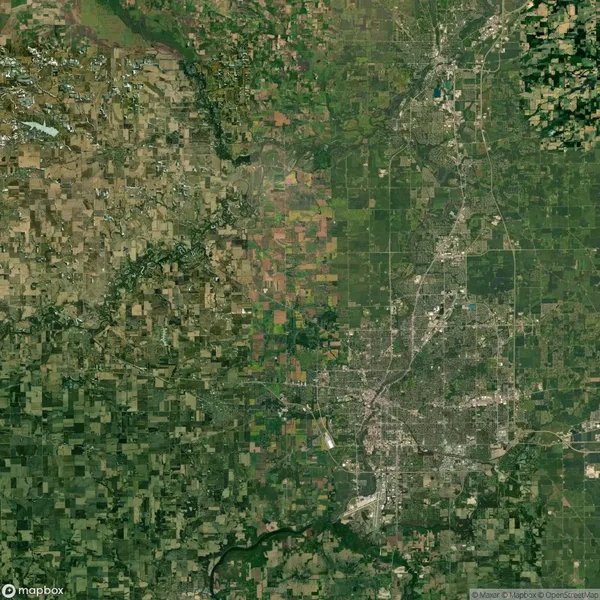 Satellite view of an extensive agricultural area on the left transitioning to a densely populated urban grid with roads and buildings on the right.