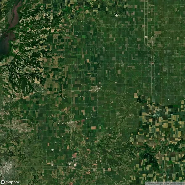 Aerial view of a vast green landscape with a patchwork of farmland and a river on the left side, showing fields of various sizes and shapes.