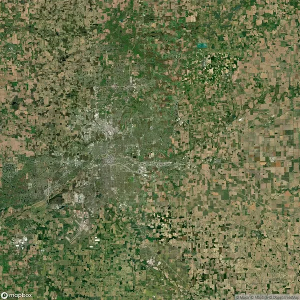 Satellite view showing a densely populated urban area surrounded by agricultural fields and greenery.