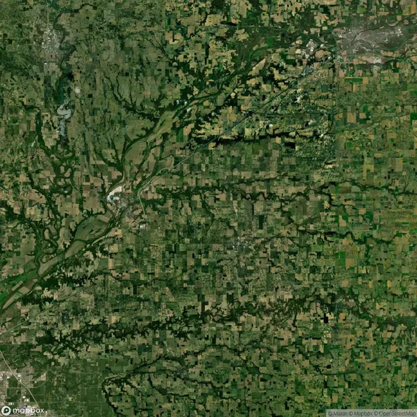 Aerial view of a landscape with a patchwork of agricultural fields, green vegetation, and a winding river flowing through the center, surrounded by small forested areas and rural developments.
