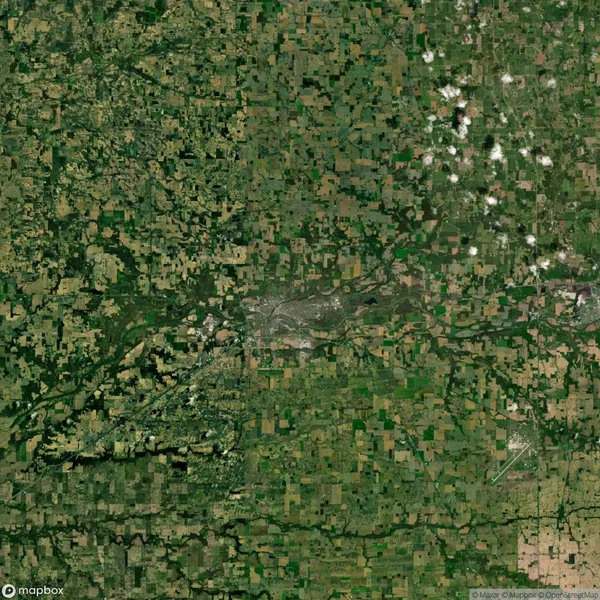 Aerial view of a rural landscape with a patchwork of green and brown fields intersected by winding roads and a river, under a partly cloudy sky.