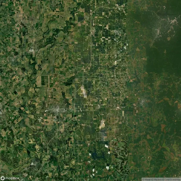 Aerial view of a large grid-like pattern of agricultural fields and sparsely populated areas, with winding rivers and patches of forests interspersed throughout the landscape.