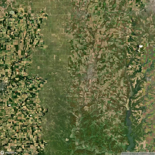 Aerial view of a landscape with a mix of agricultural fields, patches of forest, and a river winding through the bottom right. Patterns vary in color and texture.