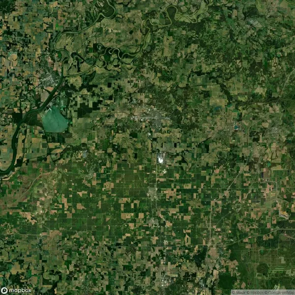 Aerial view of a patchwork landscape with farmland, roads, and a winding river in the top left. Various shades of green and brown cover the area, suggesting agricultural activity.