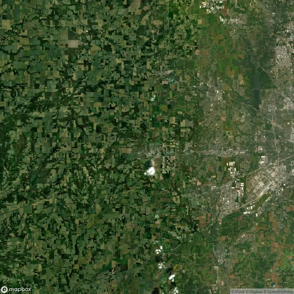 Satellite image showing a densely forested area on the left and a sprawling urban region on the right, with a visible airport and various roads connecting different zones.