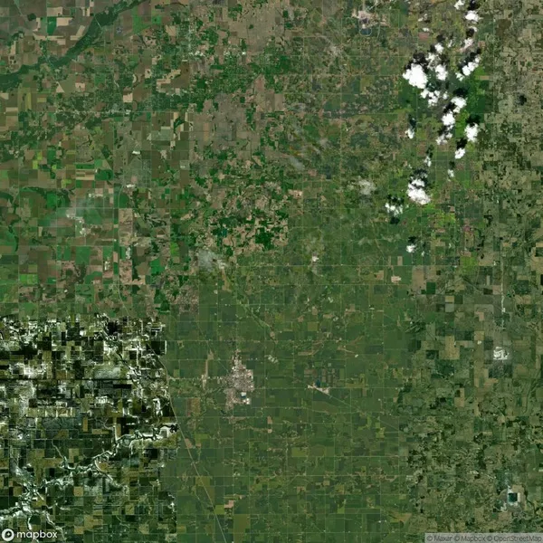Aerial view of a patchwork of green fields and farmland, interspersed with small towns and clouds in the upper right corner.