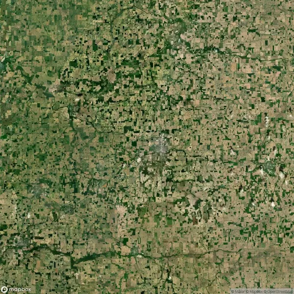 Aerial view of a vast agricultural landscape with patches of farmland, small clusters of trees, and a winding road in the center, creating a patchwork effect.