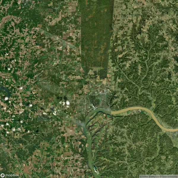 Satellite view showing a landscape with a river curving through agricultural fields and a town. Green areas and a distinct patchwork of farmland are visible, with hills on the right side.