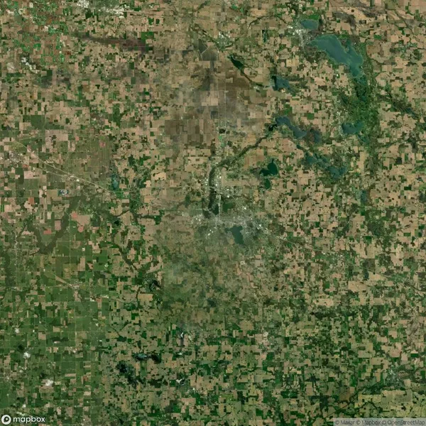 Satellite view of a landscape with a patchwork of agricultural fields, scattered green areas, and several water bodies, depicting a blend of farmland and natural elements.