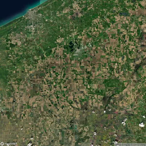 Satellite view of a landscape with a mosaic of agricultural fields, a coastline at the top left, scattered towns, and a mix of green and brown patches.