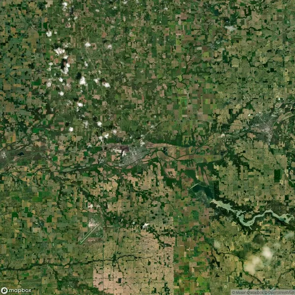 Aerial view of a landscape with a patchwork of agricultural fields, a winding river, small clouds, and a developed area in the center.