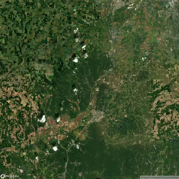 Aerial view of a landscape with dense green forest, some clouds, and patches of agricultural areas and urban development.