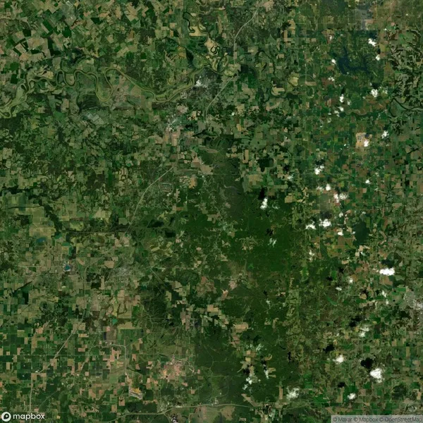 Aerial view of a large rural landscape with patchy green fields and clusters of trees. Roads and small settlements are visible among the agricultural plots.
