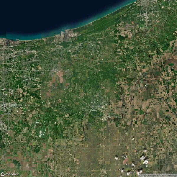 Satellite view of a coastal region showing urban areas, agricultural fields, and a body of water at the top. Various shades of green and brown indicate land use.