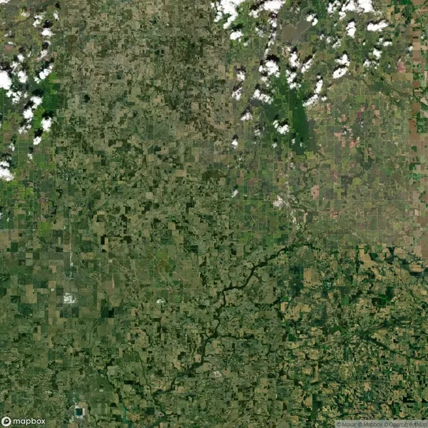 Aerial view of a rural landscape with a patchwork of green and brown fields, intersected by a dark winding river. Sparse clouds are scattered in the upper portion of the image.