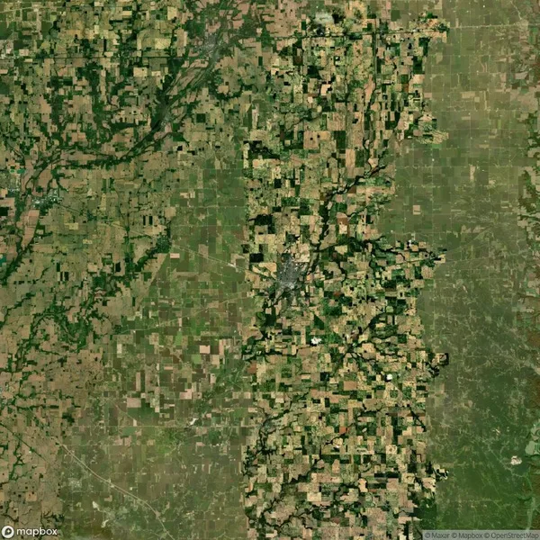 Aerial view of a landscape with a patchwork of agricultural fields, varying in size and color, intersected by roads and a green river running vertically through the center.
