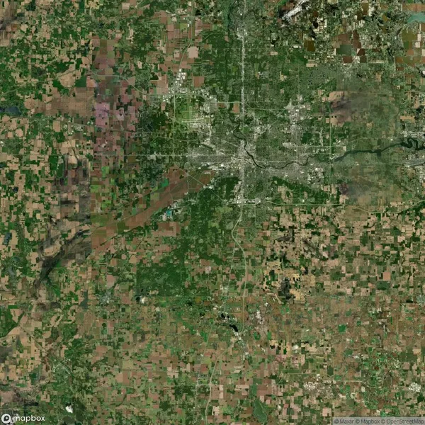 Aerial view of a sprawling urban area surrounded by farmland and patches of greenery, with a network of roads and a river running through the city.