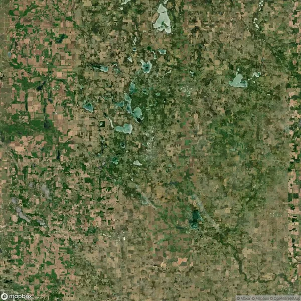 Aerial view of a patchwork landscape with various shades of green and brown, dotted with small bodies of water and intersected by roads.