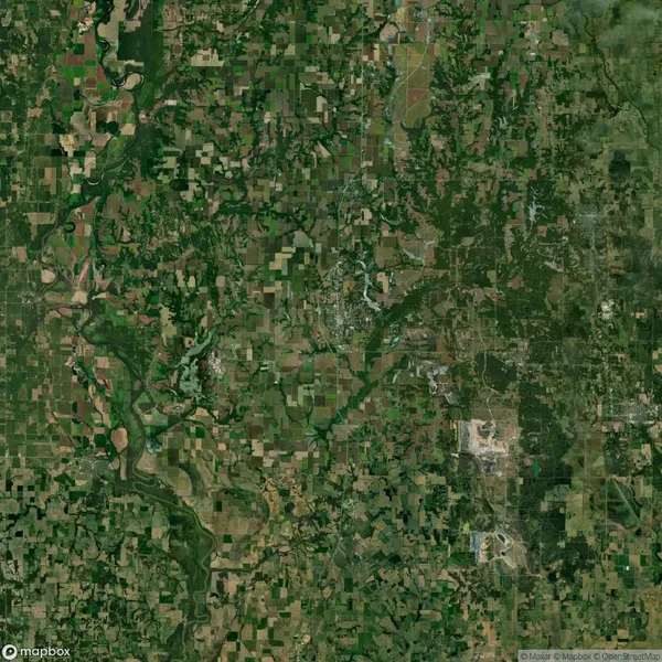 Satellite view of a large area showing a mix of green fields, forests, rivers, and developed spaces in a patchwork pattern. Roads and waterways intersect throughout.