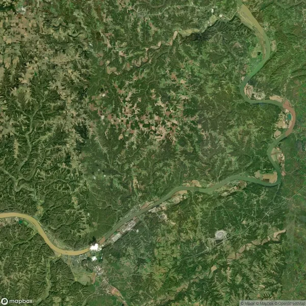Aerial view of a meandering river flowing through a landscape of lush greenery and scattered patches of farmland. A small urban area is visible along the river's path.