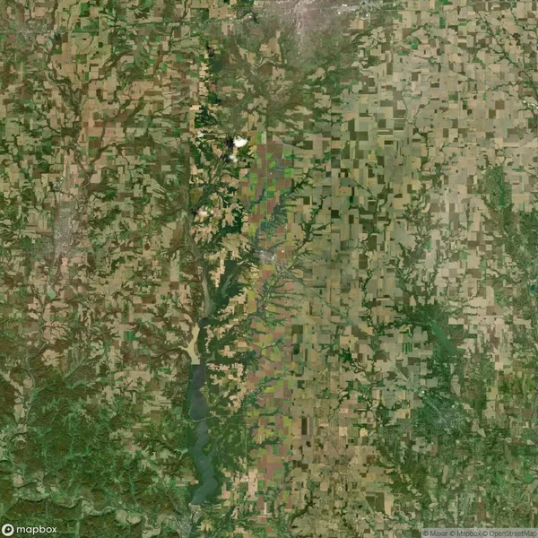 Aerial view of a vast agricultural landscape with a patchwork of fields in various shades of green and brown, divided by a meandering river. A small town is visible in the center.