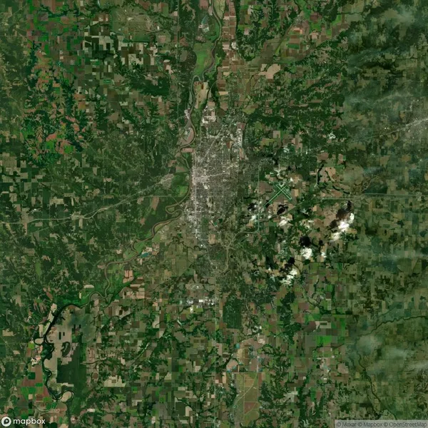 Aerial view of a green landscape featuring a river and a cityscape in the center, surrounded by fields and forests.