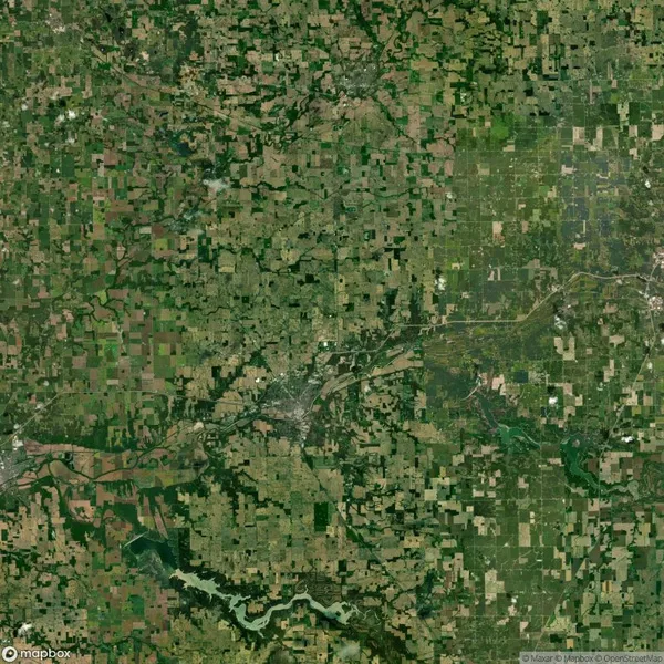 Aerial view of a vast agricultural landscape with patchwork fields, a river meandering through the center, and a mix of green and brown hues indicating various stages of crop growth.