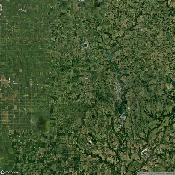 Satellite view showing a landscape with agricultural fields on the left, and a more urbanized and forested area on the right. A winding river flows through the lower right section.