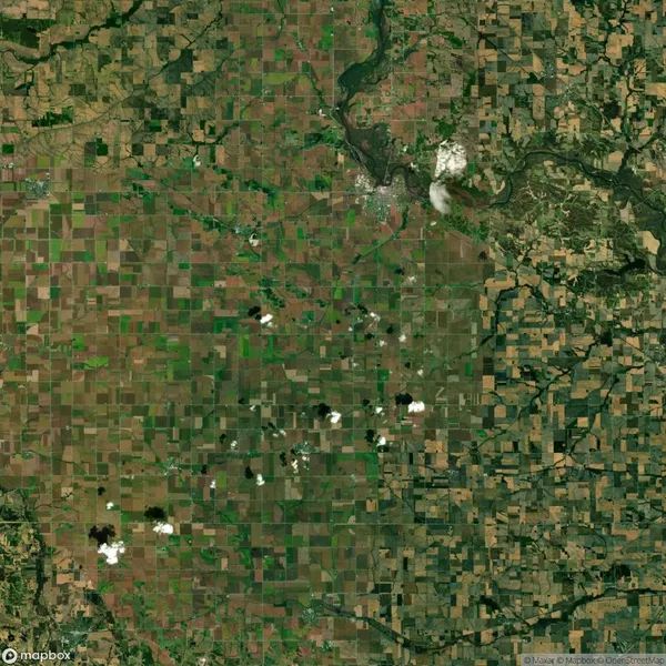 Aerial view of agricultural landscape with a grid-like pattern of fields, patches of greenery, and a winding river. Scattered clouds cast shadows over the terrain.