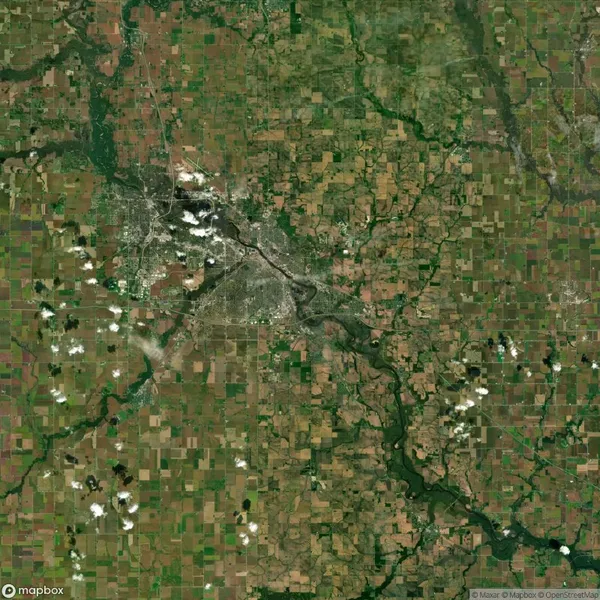 Satellite image of a landscape with a network of farms, roads, and a river running through green and brown fields, with scattered clouds overhead.
